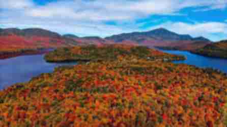 Varying colors of red, orange, yellow, and green trees surround blue lake waters with colorful mountains in the background