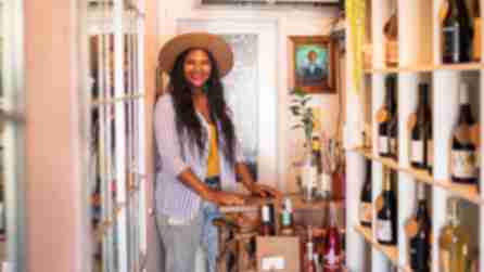 A woman posing for a picture wearing a brown fedora and a striped shirt in her wine shop at Down the Rabbit Hole
