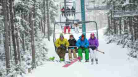 Groups of people are sitting in ski lifts traveling along the snowy tree-lined slopes at Holiday Valley