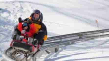 A man and child ride a coaster on rails through the snow