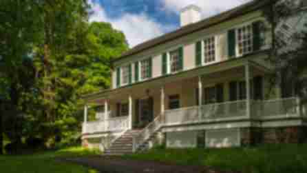 The exterior of John Jay Homestead State Historical Site on a sunny day with green foliage
