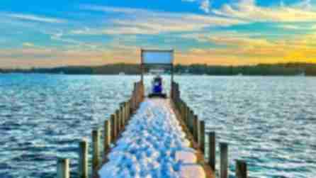 View looking out at a blue gas pump on the end of a narrow dock covered in snow on Chautauqua Lake at sunset