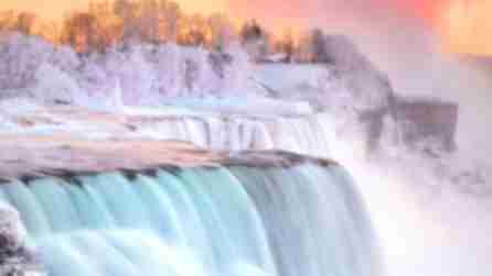 Rushing waters of Niagara Falls surrounded by snow at sunset