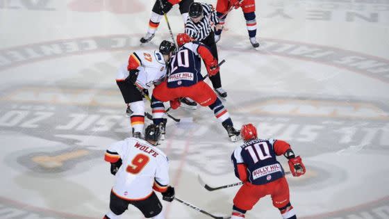 Opposing hockey players face-off on the ice as a referee drops the puck
