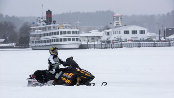 A person on a snowmobile near the boats of the Lake George Steamboat Company during the Lake George Winter Carnival