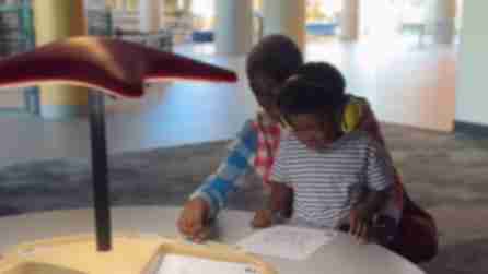 A mother and son, who has headphones on, sit at a table coloring at the Strong Museum of Play
